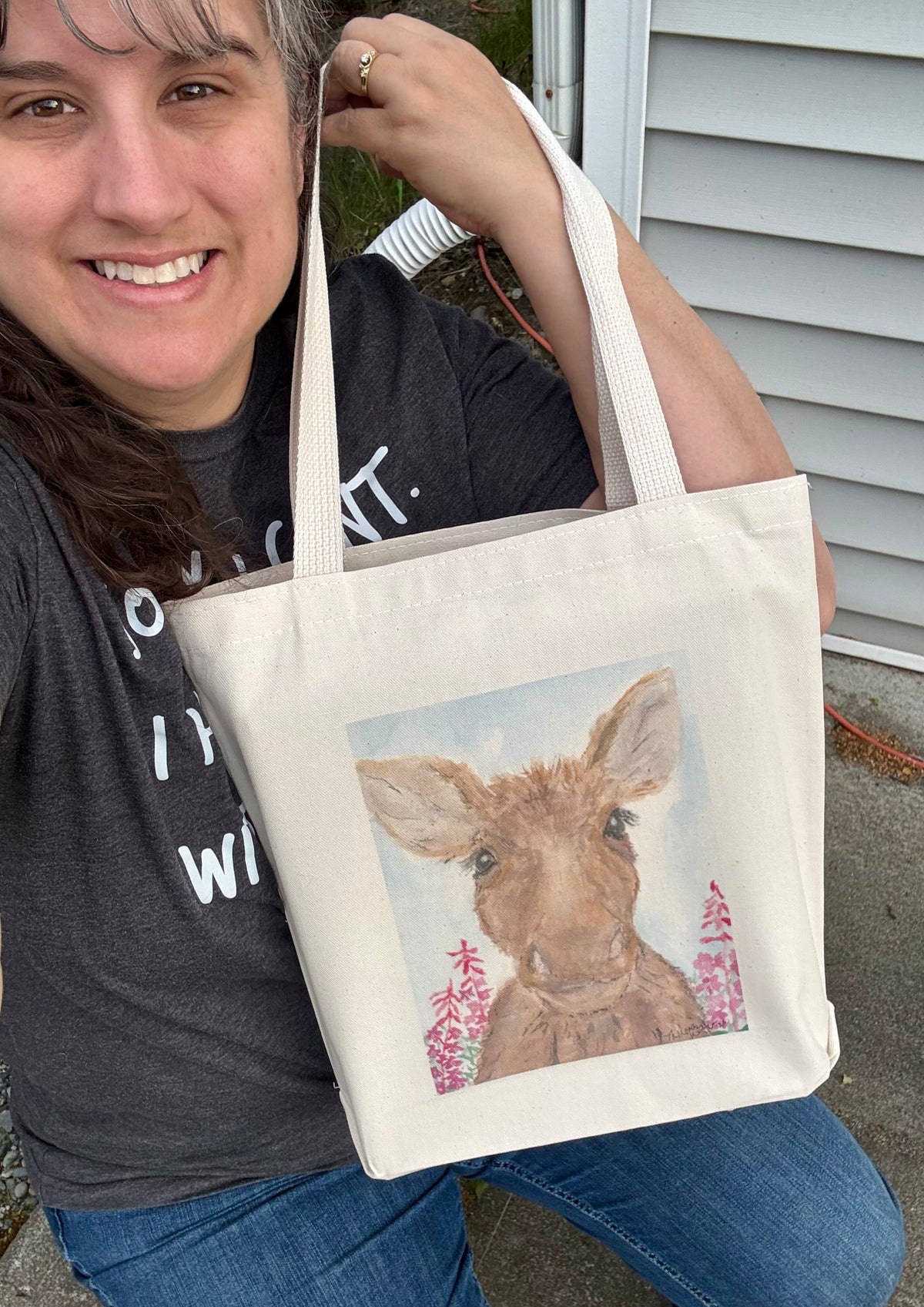 Artist Theresa Ritter holding a printed canvas bag depicting her Molly Moose painting.