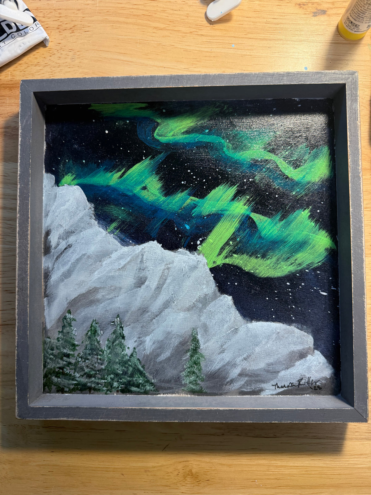 Wood panel painting of northern lights over mountain
