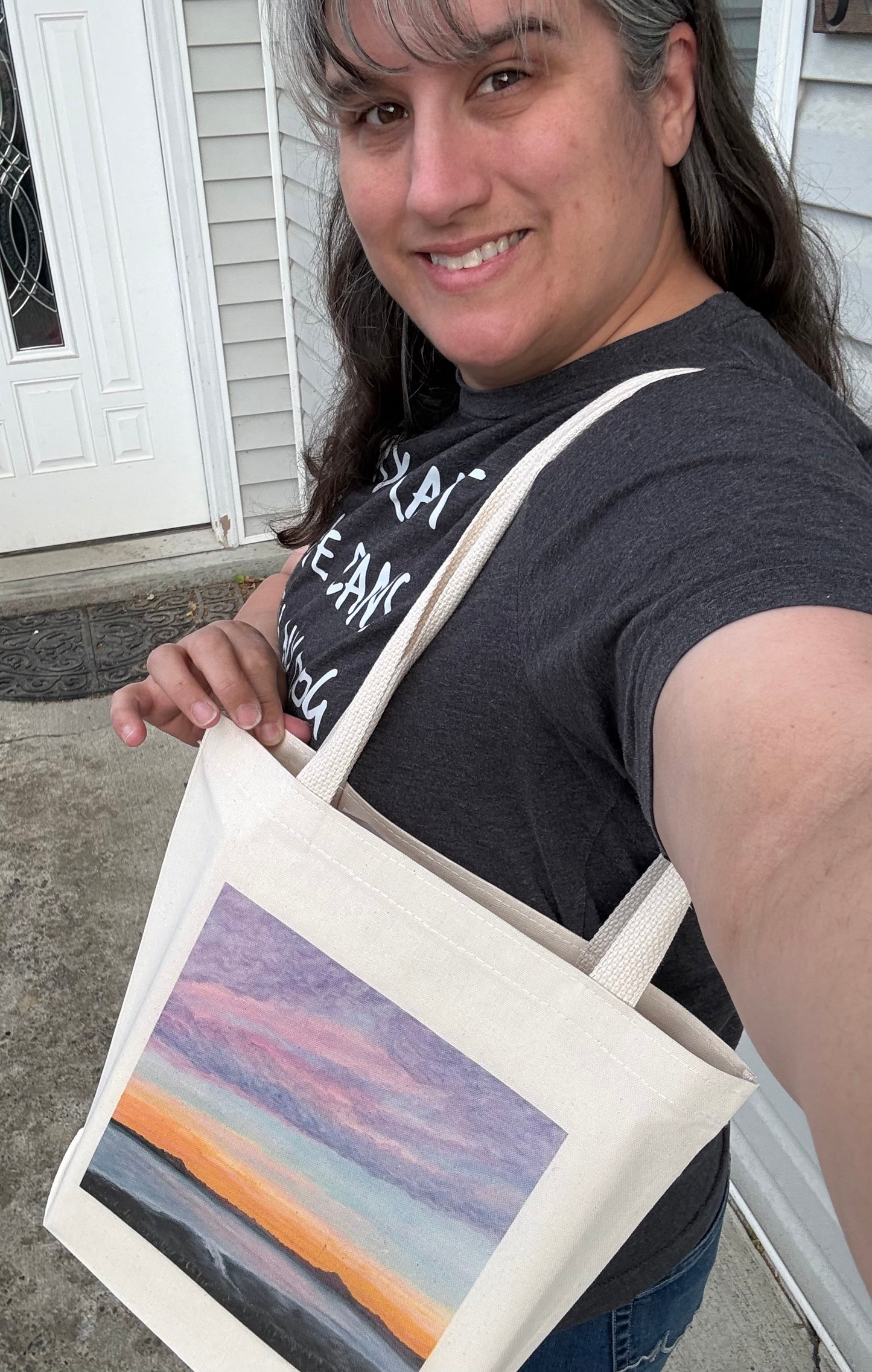 Cotton Canvas tote bag printed with October Sky an original art piece by Theresa Ritter of a sunset in  Alaska pictured with the artist holding it.